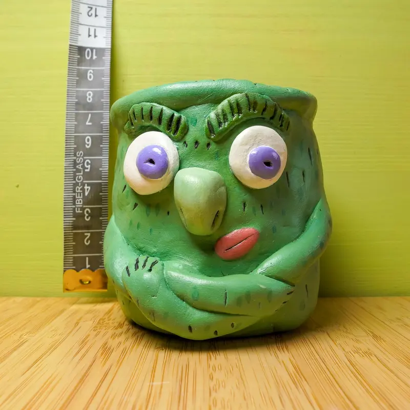 Brrr, a green clay creature with folded arms, next to a tape measure showing about 7 cm